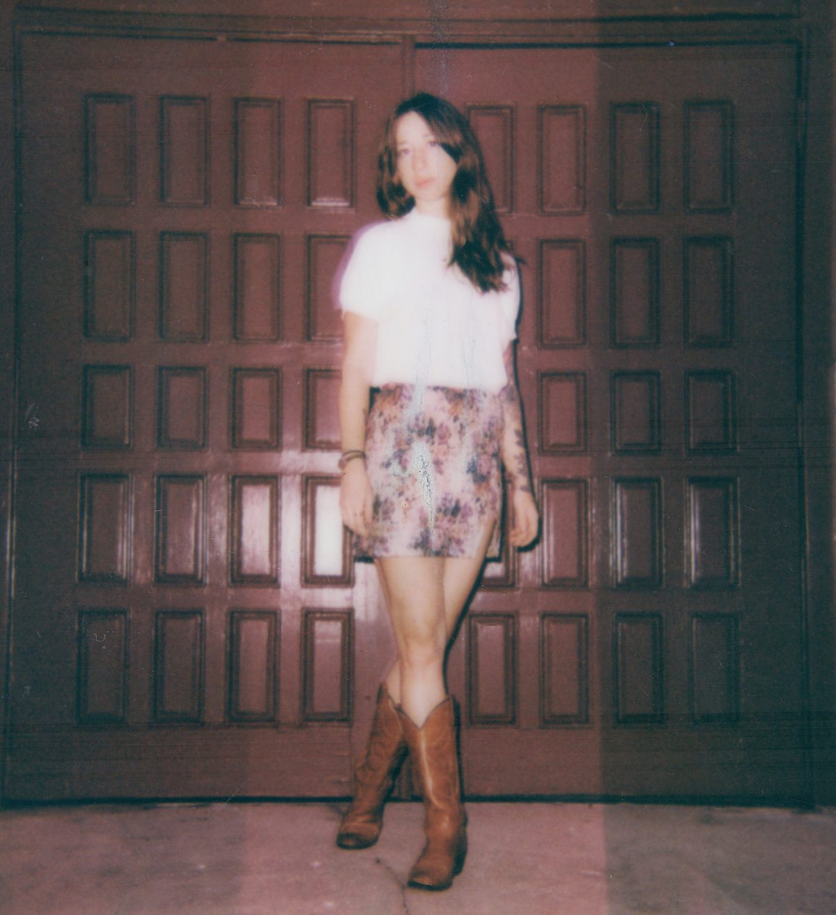 Kristen in a white tee, floral skirt and cowboy boots in front of a church door in Fort Walton
